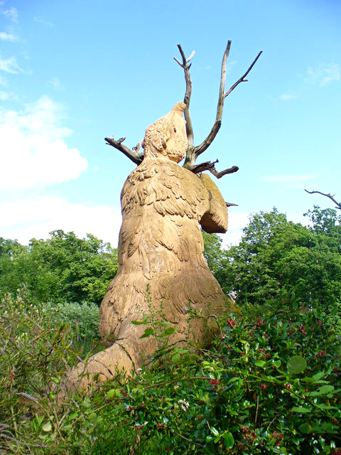 A clear photograph of the Crystal Palace Megatherium sculpture, seen from behind. It's a giant ground sloth posed sitting up beside a tree, using its tail as a tripod and with its arms wrapped around the trunk. It has a short nose trunk and a coat of shaggy fur.