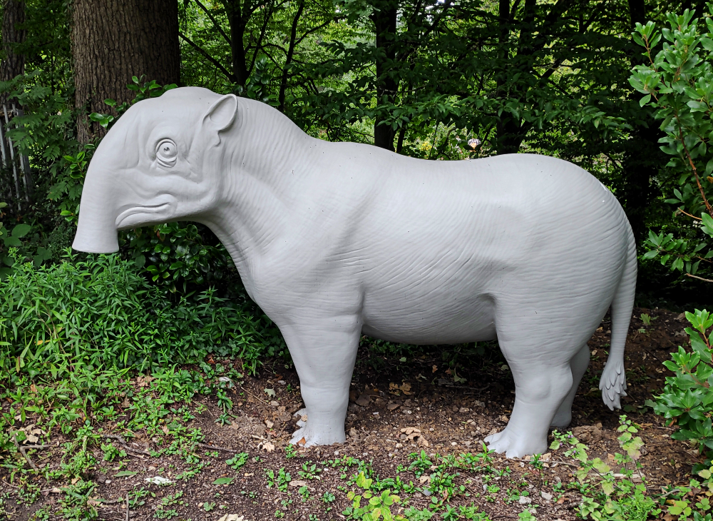 A photograph of the restored Crystal Palace Palaeotherium magnum statue. It's a chunky animal with a trunked tapir-like head, wrinkly skin, and a rhino-like body.